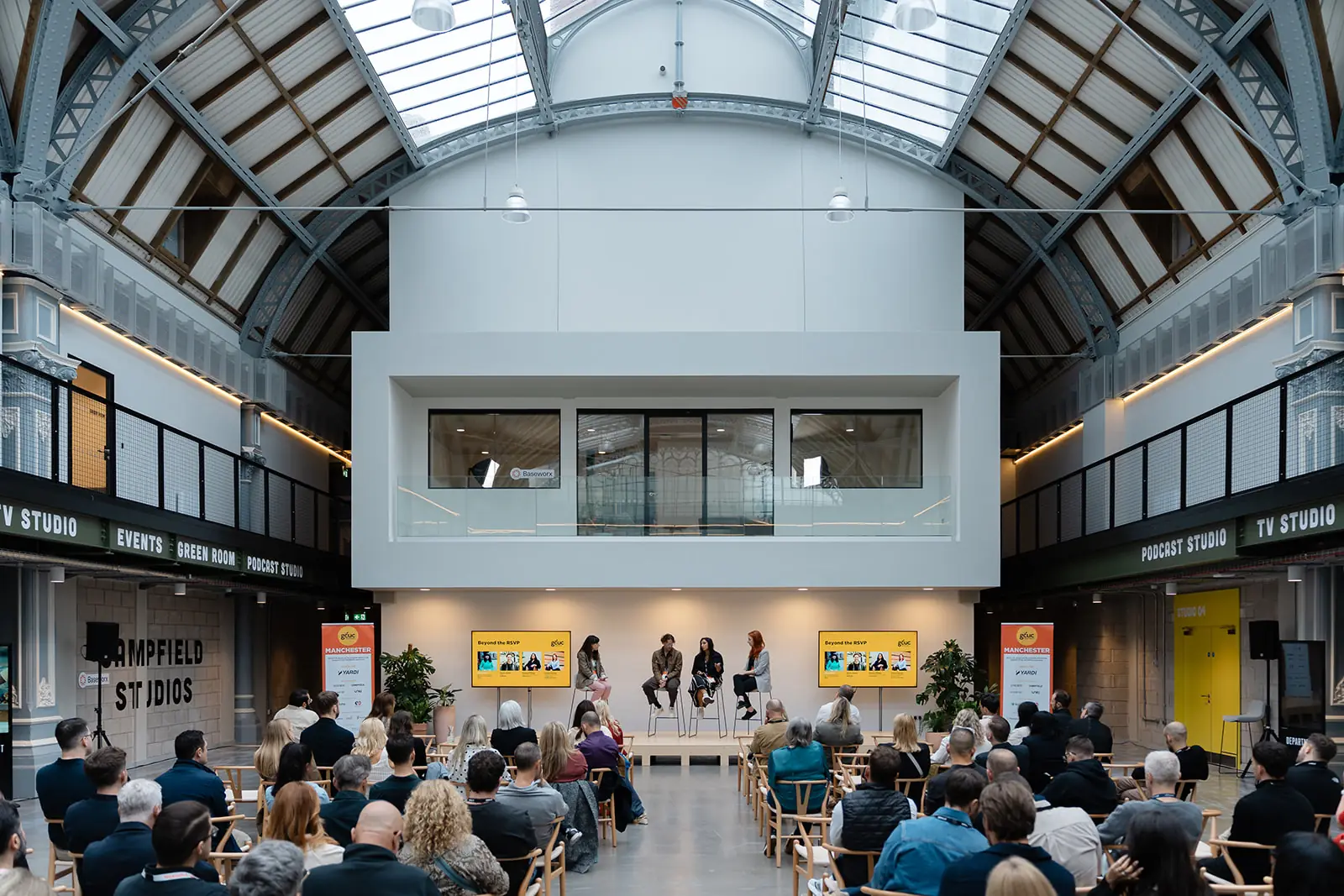 Delegates seated in a daylit Manchester atrium watching a four-person GCUC panel on stage